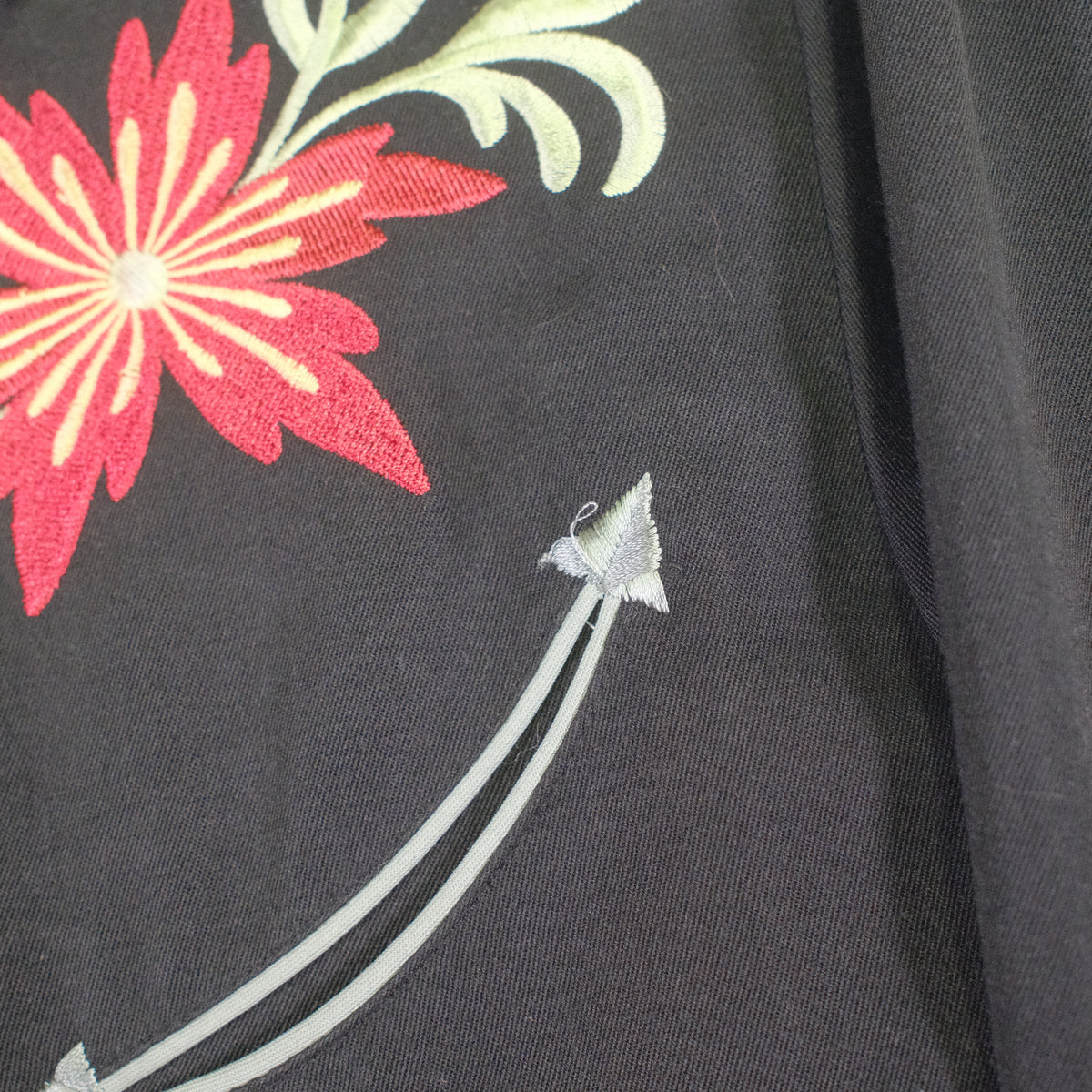 Close-up of a black fabric surface with a large red floral embroidery and pale green leaves, plus a small light gray stitched accent.